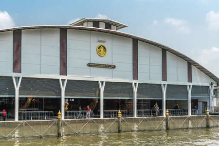 Bangkok city, Thailand - March 17, 2019: Royal Barge National Museum. White Front facade with gold emblem and text has boat access to Bangkok Noi Canal. LIght blue sky on top, greenish water up front.のeditorial素材