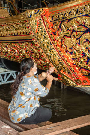 Bangkok city, Thailand - March 17, 2019: Royal Barge National Museum. Closeup of woman maintaining withc hammer and chisel the golden decorations on side of barge.のeditorial素材