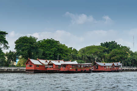 Bangkok city, Thailand - March 17, 2019: Chao Phraya River. Group of red barge boats on the water in front of park of Saifee Mosque under light blue sky.のeditorial素材
