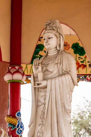 Si Racha, Thailand - March 16, 2019: Closeup of Gray statue of Guan Yin at her open circular shrine on Ko Loi Island. Backed by reds, beiges and whites.のeditorial素材