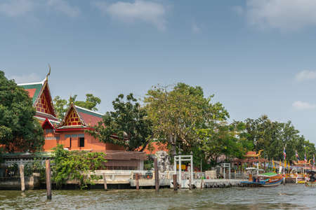 Bangkok city, Thailand - March 17, 2019: Bangkok Noi Canal. Docks with boats at Wat Suwannaram Ratchaworawihan Buddhist temple under blue sky and partly hidden by green trees.のeditorial素材