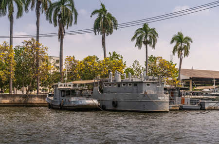Bangkok city, Thailand - March 17, 2019: Bangkok Noi Canal. Group of gray police boats docked together under palmtrees and yellow flowers.のeditorial素材