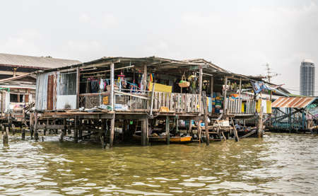 Bangkok city, Thailand - March 17, 2019: Bangkok Noi Canal. Dilapidated poor housing built on stilts in the greenish water offers chaotic view under silver sky.のeditorial素材