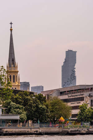 Bangkok city, Thailand - March 17, 2019: Chao Phraya River. Holy Rosary Church with green foliage under silver sky. In back, King Power MahaNakhon special architecture skyscraper.のeditorial素材