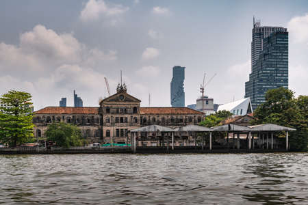 Bangkok city, Thailand - March 17, 2019: Chao Phraya River. Dilapidated Old Customs House , brown stones blackened bay mold under cloudscape. Iconic skyscraper King Power MahaNakho in back.のeditorial素材