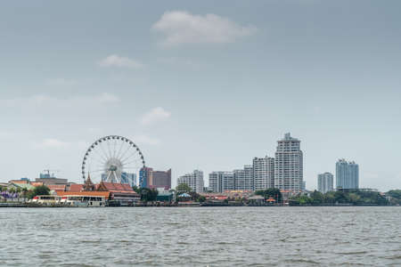 Bangkok city, Thailand - March 17, 2019: Chao Phraya River. Wide shot with Chang Ferris Wheel and entertainment park. Tall residential buildings on horizon. Light blue sky with cloudscape..のeditorial素材