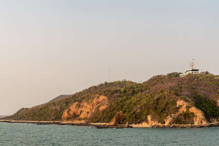Laem Chabang seaport, Thailand - March 17, 2019: White building of port control and operation center in brown-green hills above the harbor with antennas and under sunset light. Sea in front.のeditorial素材