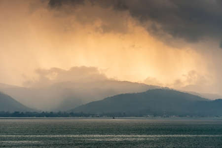 Ko Samui Island, Thailand - March 18, 2019: Sunrise over the hills paints orange to yellow canvas in the dense clouds. Dark sea water in front with Nathon port area on shore.の写真素材