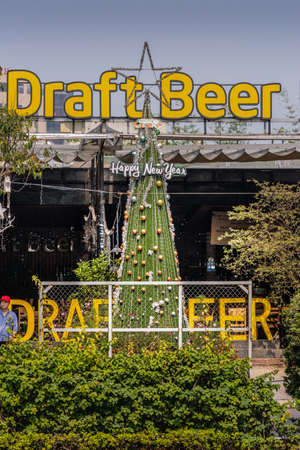 Da Nang, Vietnam - March 10, 2019: Giant yellow sign for Draft Beer at bar near Memorial Park under blue sky with lots of green foliage. Second sign reads Happy New Year.のeditorial素材