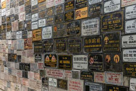 Da Nang, Vietnam - March 10, 2019: Wall of Thank You plaques at Virgin Mary grotto outside Cathedral. Mostly white, black, gold, and red.のeditorial素材