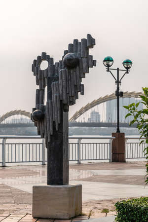Da Nang, Vietnam - March 10, 2019: Han River Boardwalk art exhibition. Black marble non-figurative statue with tall buildings and bows of dragon bridge in back.のeditorial素材
