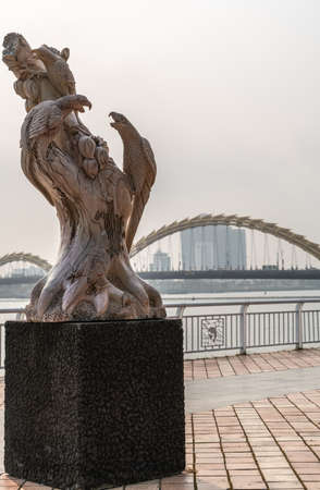 Da Nang, Vietnam - March 10, 2019: Han River Boardwalk art exhibition. Brown tree with parrots statue with tall buildings and bows of dragon bridge in back.のeditorial素材