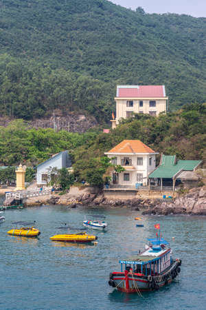 Nha Trang, Vietnam - March 11, 2019: Closeup of traditional colored ferry boat anchored in marina with other smaller pleasure crafts. Shore has houses and back is forested hill side.のeditorial素材