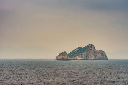 Nha Trang, Vietnam - March 11, 2019: Rock island in South China Sea at entrance to harbor of the town. Foggy morning sky and gray blue sea water.の写真素材