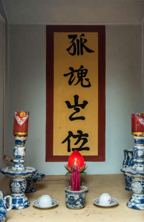 Nha Trang, Vietnam - March 11, 2019: Dinh Phu Vinh community center and celebration hall. Niche with red lotus candle in front of black mandarin text on yellow, painted on wall.のeditorial素材