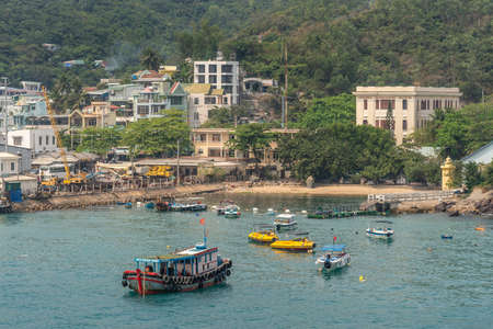 Nha Trang, Vietnam - March 11, 2019: Ferry landing pier with colorful small boats in marina adjacent to commercial port. Hotels and housing against green hill flank.のeditorial素材