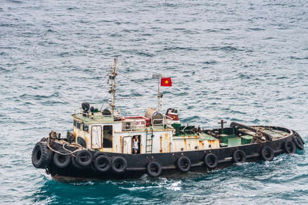 Nha Trang, Vietnam - March 11, 2019: Evening, closeup of tugboat with skipper visible and national flag  on greenish sea water.のeditorial素材