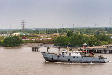 Long Tau River, Vietnam - March 12, 2019: Phuoc Khanh area. Phu Quy 07 is gray and white crew delivery and supply ship able to take cargo, too. People on board. Green foliage in back under light blue sky.のeditorial素材