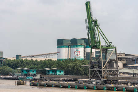 Long Tau River, Vietnam - March 12, 2019: Phuoc Khanh area. Closeup of Cong Thanh Group cement factory with its silos, transport belt. and quays to handle ships under blue sky and behind brown water.のeditorial素材