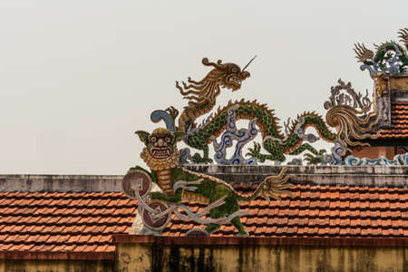 Nha Trang, Vietnam - March 11, 2019: Dinh Phu Vinh community center and celebration hall. Closeup on corner piece of Dragon statues as decorations on red roof against silver sky .のeditorial素材
