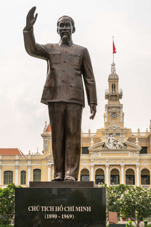 Ho Chi Minh City, Vietnam - March 12, 2019: Downtown. Town Hall or Peopleâs Committee of HCMC French style building with clock tower behind bonze statue of Ho Chi Minh himself under silver sky.のeditorial素材