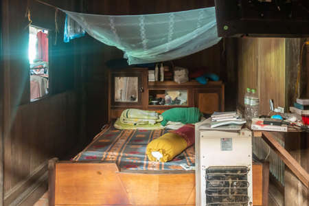 Cai Be, Mekong Deltal, Vietnam - March 13, 2019: Small bedroom with office table and white refrigerator. Azure Mosquito net above bed. Small window makes room rather dark.のeditorial素材