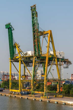 Ho Chi Minh City, Vietnam - March 13, 2019: Ben Nghe port on Song Sai Gon river at sunset. Green-yellow idle container cranes on quay with modern high rise residential buildings on horizon.のeditorial素材