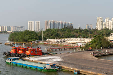 Ho Chi Minh City, Vietnam - March 13, 2019: Vict port on Song Sai Gon river at sunset. 3 idle red tugboats at quay, Residential high rise buildings in back. Light blue sky and green belt.のeditorial素材