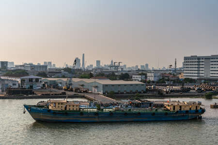 Ho Chi Minh City, Vietnam - March 13, 2019: Song Sai Gon river at sunset. Blue Hoang Long 01 river tanker on side fueling other vessel near pier, quay and yard with warehouses and rolls of steel plate.のeditorial素材