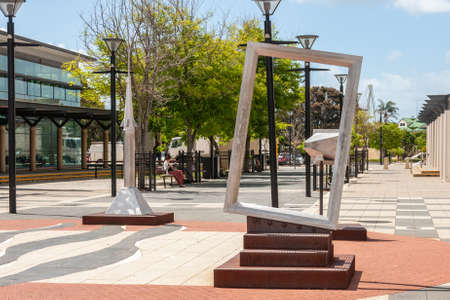 Mandurah, WA, Australia - November 25, 2009: simple artwork in almost empty The Boardwalk shopping mall under light blue sky and with green foliage. One woman reads on bench.のeditorial素材