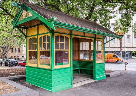 Melbourne, Australia - November 16, 2009: Green and yellow waiting room, locale for the public trams under green tree. Doorless opening and windows in three walls Street scene with cars.のeditorial素材