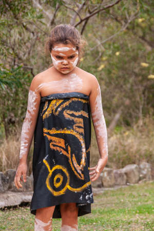 Newcastle, Australia - December 10, 2009: Closeup of young Aboriginal girl dressed in black dress with yellow traditional drawings, and her body painted with white stripes. Green foliage,のeditorial素材