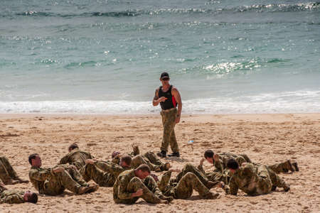 Newcastle, Australia - December 10, 2009: Group of camouflage clad young Australian Marines exercise stomach crunches on sandy beach at greenish water edge. Instructor present.のeditorial素材