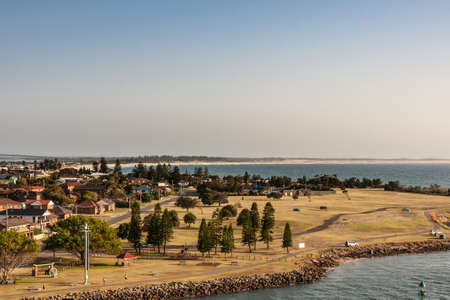 Newcastle, Australia - December 10, 2009: Looking over Stockton peninsula with its South Pacific shoreline forming a bow on the horizon under light blue to silver sky. Green foliage in front.の写真素材