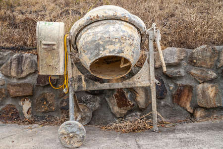 Closeup of idle filthy beige and gray small electrical cement mill on wheels parked along short...