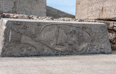 Newcastle, Australia - December 10, 2009: Fisherman with sloop in bottle artwork edged on defensive large gray stone on Nobbys breakwater pier.のeditorial素材
