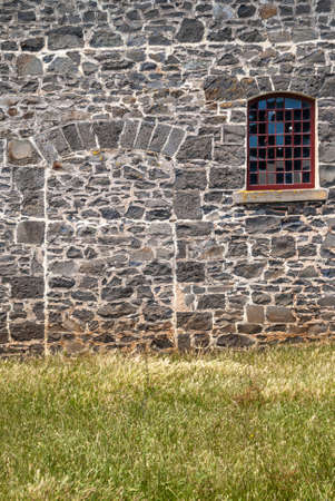 Stanley, Tasmania, Australia - December 15, 2009: Hightfield Historic Site. Closeup of Filled-in doorway on gray stone building ruins with green lawn in front and small broken glass window.の写真素材