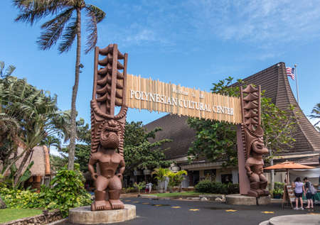 Laie, Oahu, Hawaii, USA. - January 09, 2020: Polynesian Cultural Center. Monumental gate into the park with brown giant aboriginal statues. People and green vegetation under blue sky.のeditorial素材