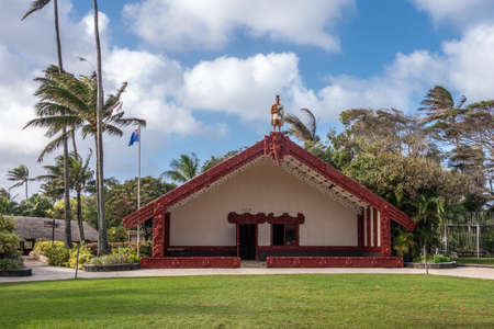 Laie, Oahu, Hawaii, USA. - January 09, 2020: Polynesian Cultural Center. Grand hall with maroon frames and warrior statue on top of the New Zealand Maori people under blue cloudscape. Green by foliage and lawn.のeditorial素材