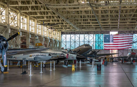 Oahu, Hawaii, USA. - January 10, 2020: Pearl Harbor Aviation Museum. Line of airplanes in hangar with large USA flag in back. Beige roof. Natural light through windows.のeditorial素材