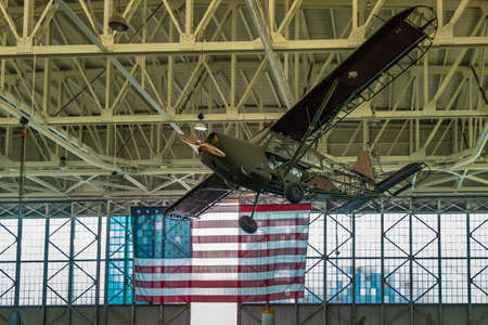 Oahu, Hawaii, USA. - January 10, 2020: Pearl Harbor Aviation Museum. small green airplane hangs from beige ceiling. Natural light through windows. Huge USA flag.のeditorial素材