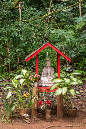 Kaneohe, Oahu, Hawaii, USA. - January 11, 2020: Small red shrine for white Bodhisattva statue in garden of Byodo-In Buddhist temple. Greeen foliage background, flowers and plants in front.の写真素材