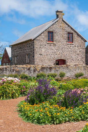 Stanley, Tasmania, Australia - December 15, 2009: Hightfield Historic Site. Flower garden adds color in front of gray stone house under blue cloudscape.のeditorial素材