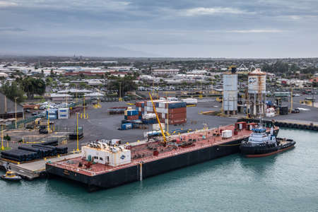 Kahului, Maui,, Hawaii, USA. - January 13, 2020: Nale double hull liquid tank barge docked at container quay in azure water port under light blue cloudscape. Buildings of town in back.のeditorial素材