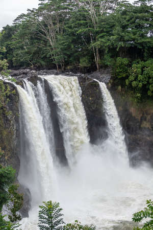 Hilo, Hawaii, USA. - January 14, 2020: Closeup of White Rainbow Falls itself on foaming violent Wailuku River surrounded by green trees and plants.の写真素材
