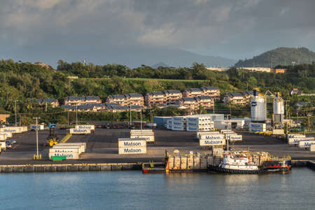 Nawiliwili, Kauai, Hawaii, USA. - January 16, 2020: Early morning light on dock in the port with Matson container yard. Green tree belt and houses in back under brown and light blue sky. Tugboat and barge.のeditorial素材