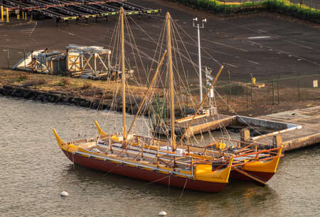 Nawiliwili, Kauai, Hawaii, USA. - January 16, 2020: Early morning light on yellow and maroon Namahoe replica of Pacific Islands Long Distance Canoe upon blue ocean water,のeditorial素材