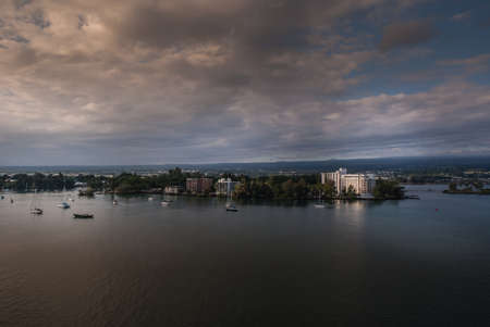 Hilo, Hawaii, USA. - January 9, 2012: White Grand Naniloa Hotel in green park on shore at nightfall, sunset.. Dark blrown cloudscape over dark ocean water. Few sail boats anchored.のeditorial素材