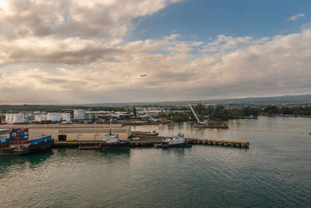 Hilo, Hawaii, USA. - January 9, 2012: Sunset over harbor with white brown cloudscape with blue patches and an aircraft leaving airport in back. Boats, warehouses and fuel tanks.のeditorial素材
