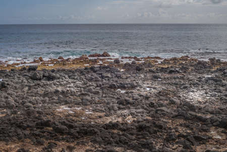 Kauai, Hawaii, USA. - January 11, 2012: Black lava rocks at Kawailoa beach in front of azure and gray ocean under light blue sky with far away clouds.の写真素材